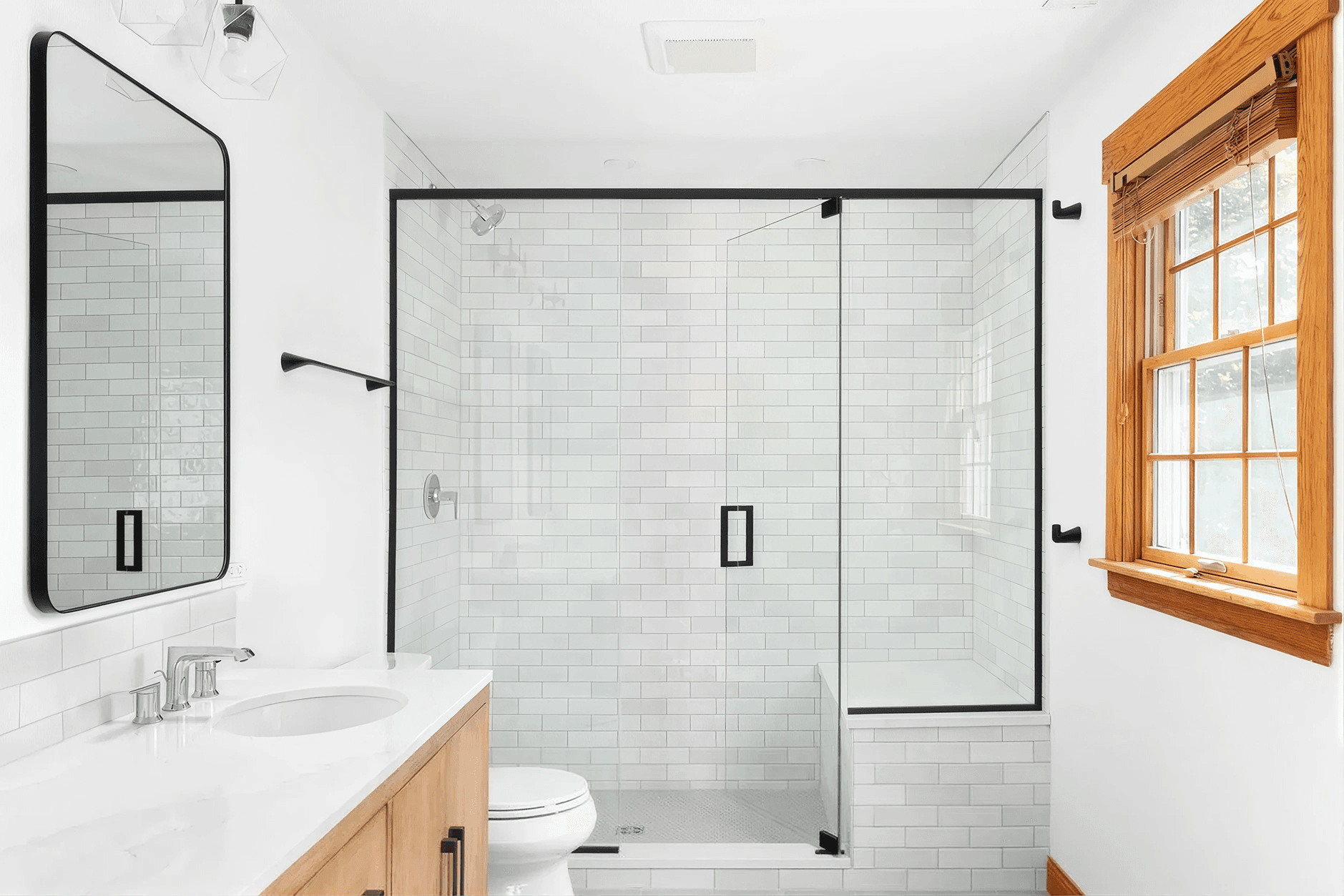 Bright modern bathroom featuring a white subway tile walk-in shower with glass enclosure, wood vanity, large mirror, and chrome fixtures.