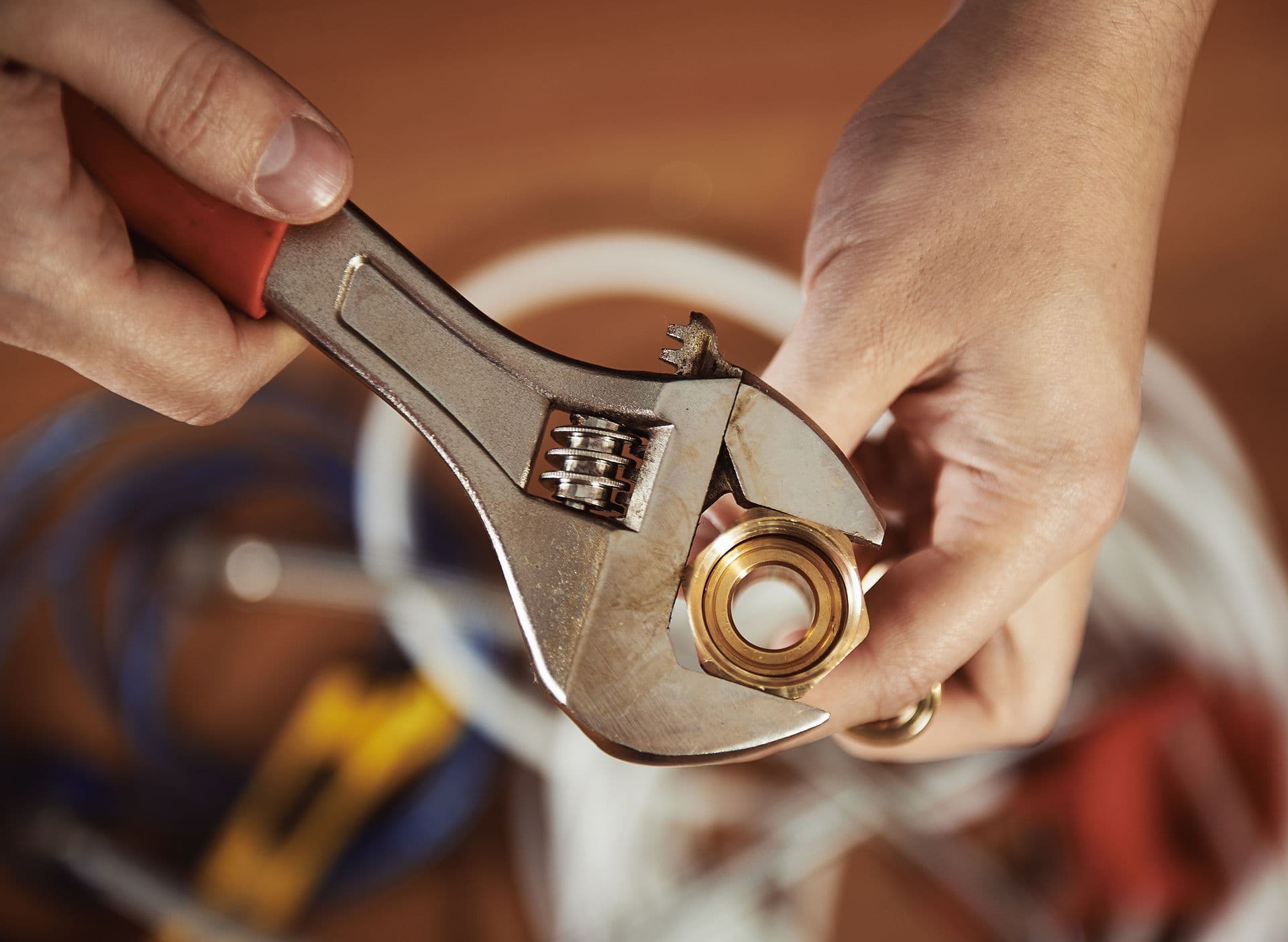 Close-up of plumber hands screwing nut of pipe with wrench over plumbing tools background. Concept of repair and technical assistance.
