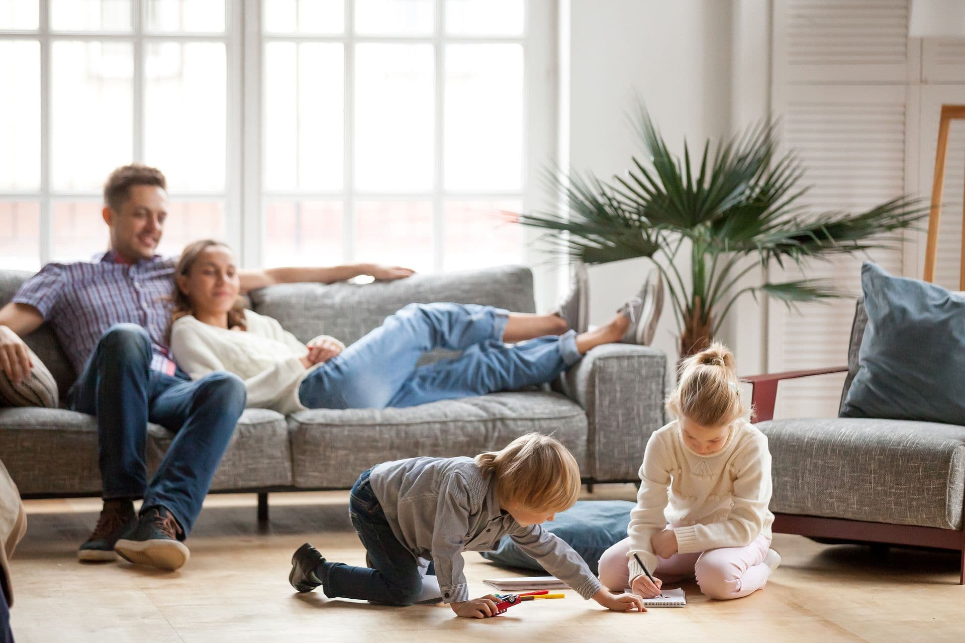Family relaxing together in a bright living room while two children play on the floor, illustrating a comfortable, healthy home environment.
