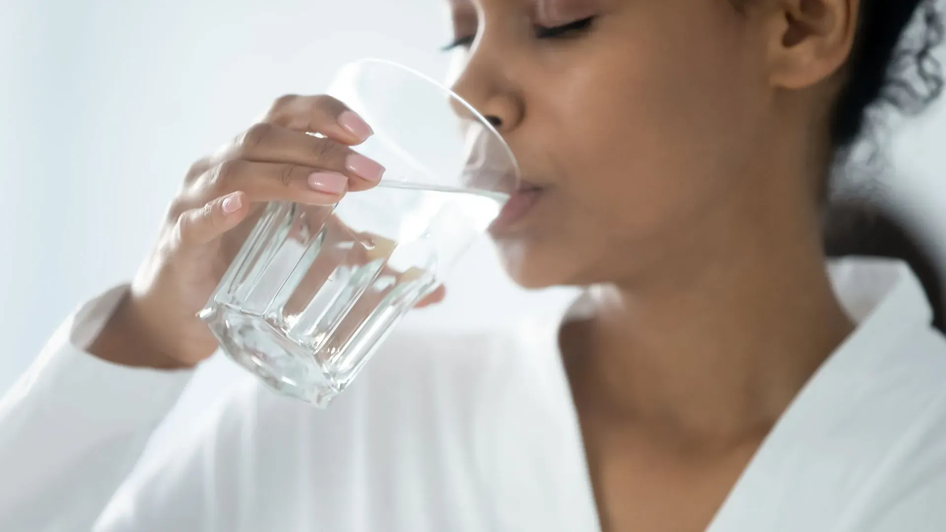 Person drinking a glass of clean, filtered water, highlighting healthy hydration and access to safe drinking water at home.
