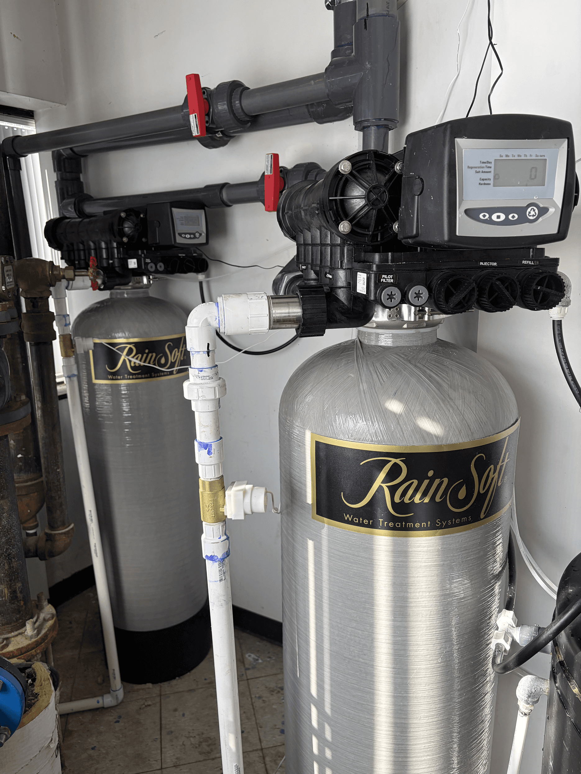 Commercial RainSoft water treatment system with dual filtration tanks, digital control valves, and industrial plumbing connections for high-capacity water treatment.
