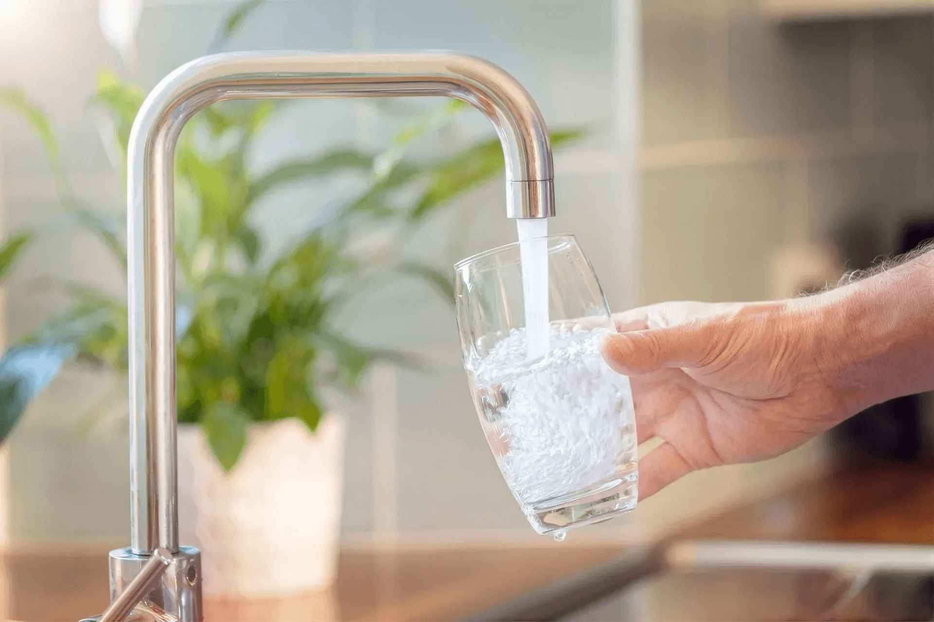 Hand filling a glass with fresh drinking water from a modern kitchen faucet, representing clean, filtered water for everyday hydration and healthy living at home.
