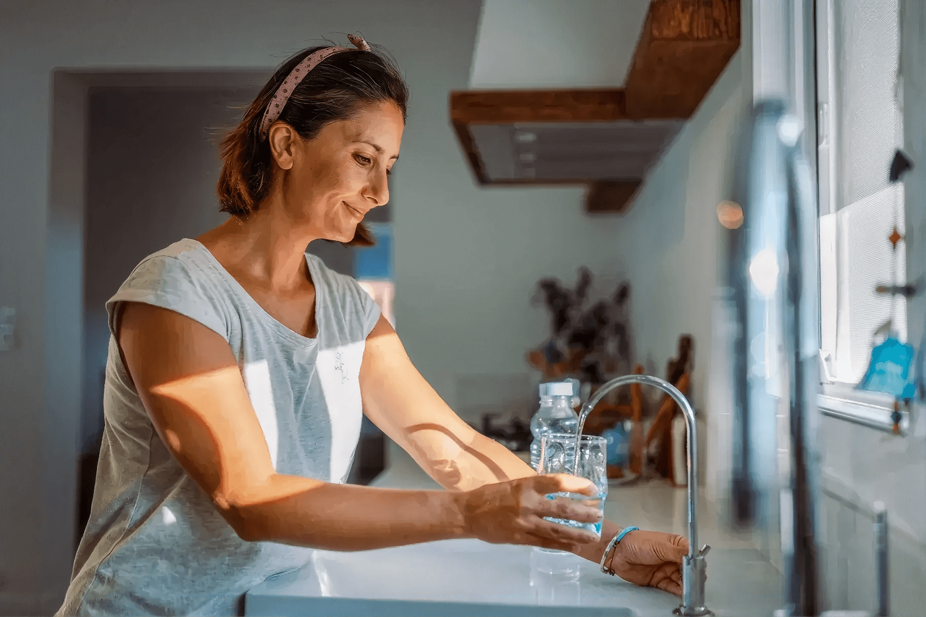 Person filling a drinking glass with fresh tap water from a modern kitchen faucet in a bright home kitchen, highlighting clean, filtered drinking water.