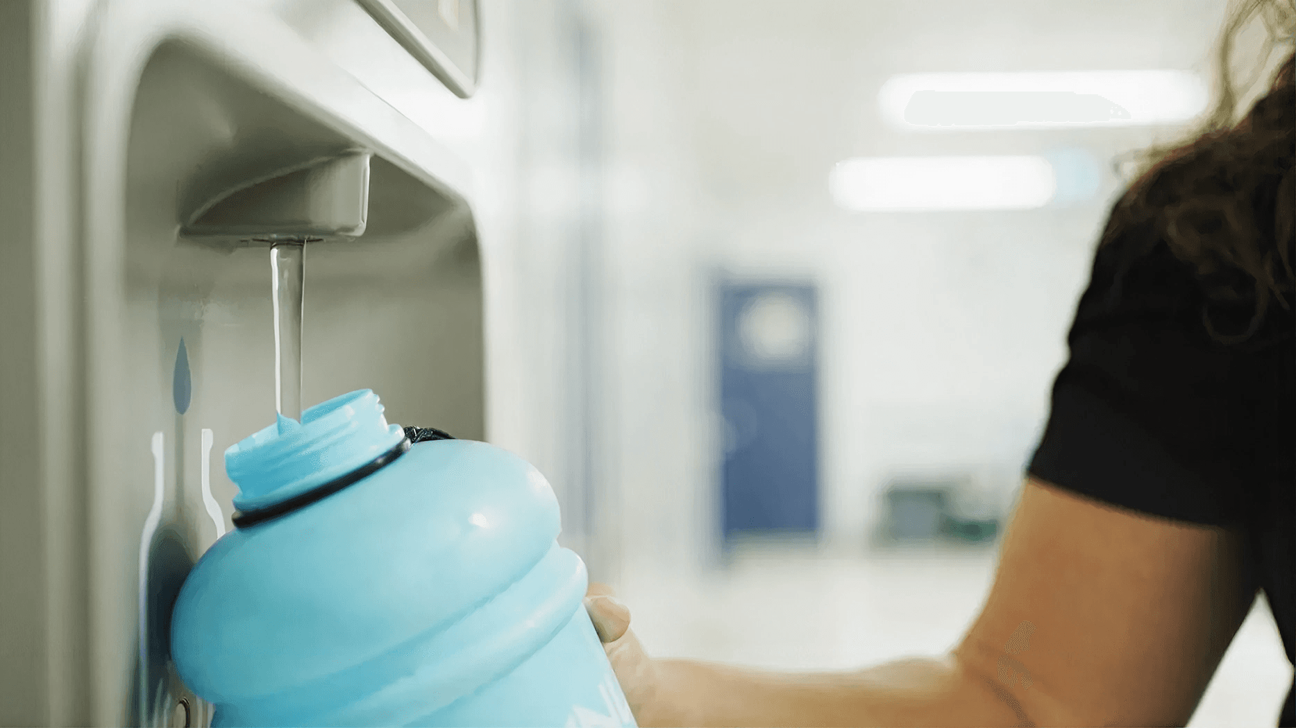 Person refilling a reusable water bottle at a filtered water bottle filling station, promoting convenient access to clean drinking water.