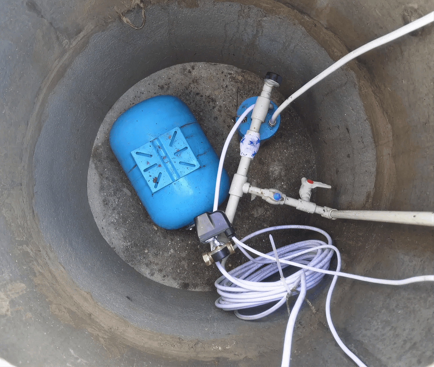 Pressure tank and well water supply components installed inside a residential well pit, including plumbing lines, pressure controls, and shutoff valves for a private well system.